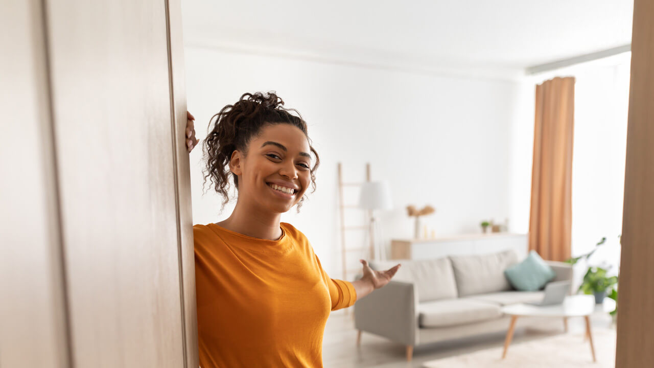 A young woman with medium-complexion and yellow shirt invites us into her home