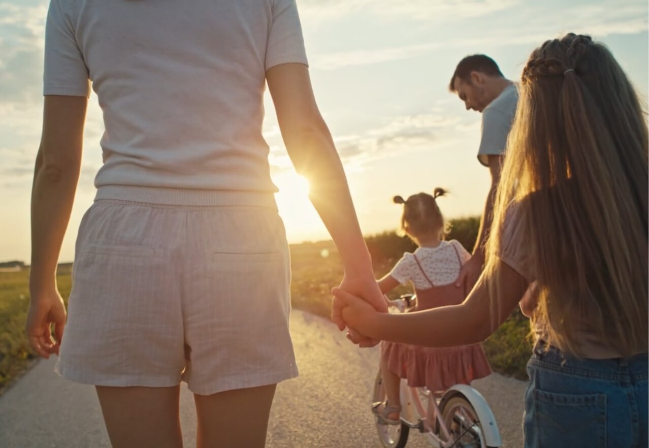 family walking and riding bikes on a path at sunset