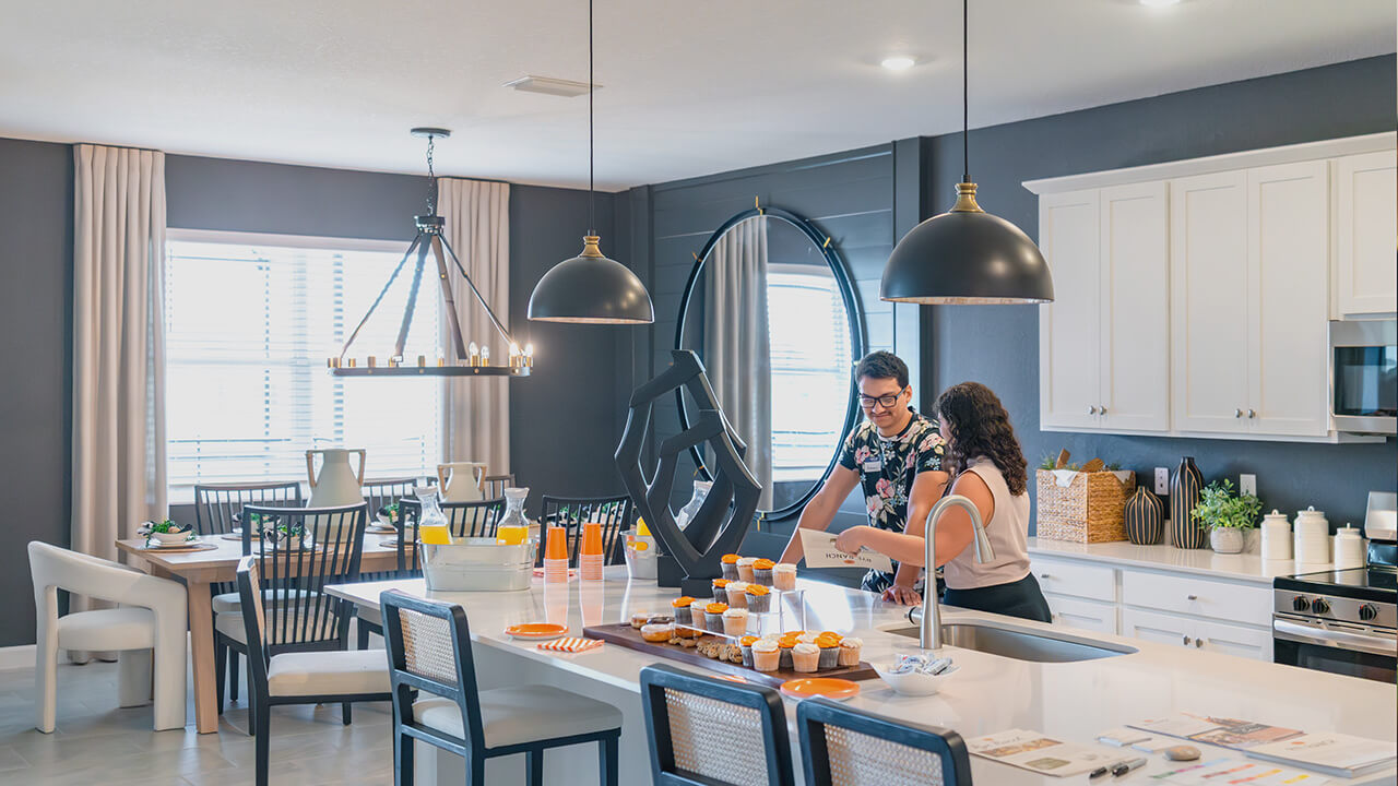 a man and woman stand smiling around a kitchen island, setting up for a party - They represent two people investing in Southwest Florida real estate